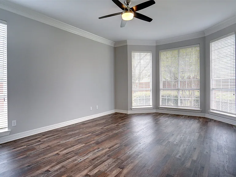 Spacious room featuring wood-finish flooring, light gray walls, and white crown molding