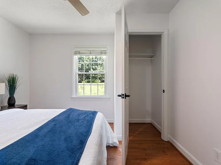 Well-proportioned bedroom with a large window for natural light, hardwood floors, ceiling fan, and a closet for storage.