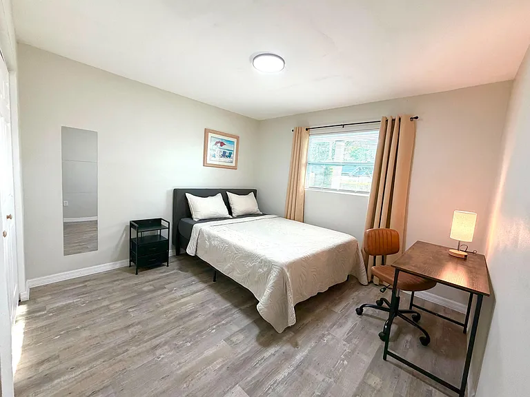 Furnished bedroom with a full bed, desk workspace, and window with curtains, plus durable wood-look flooring.