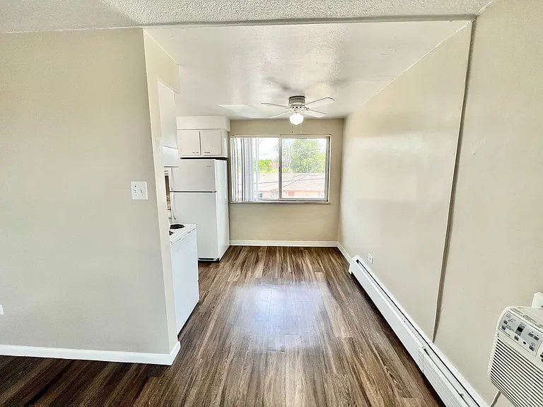 Bright and airy kitchen area with sleek flooring, modern white appliances, and a large window overlooking greenery.