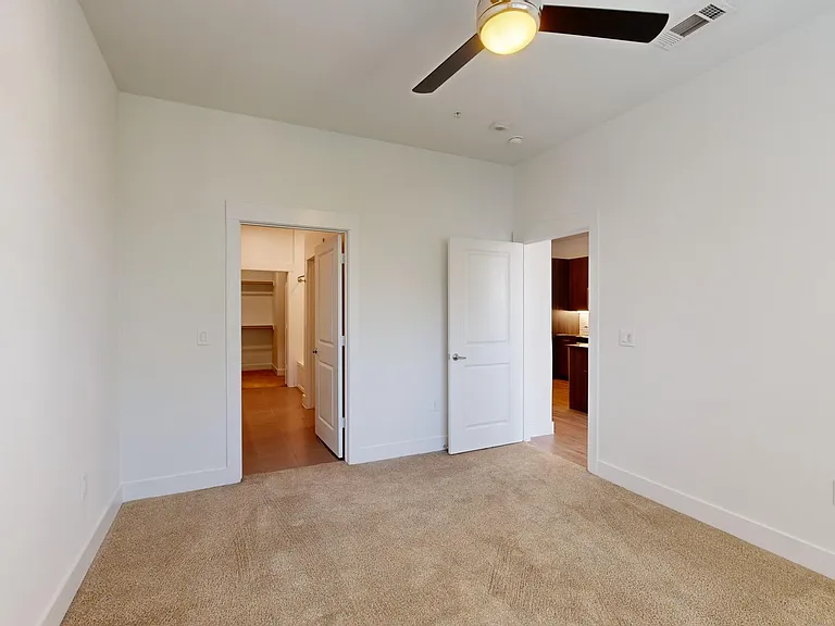 Spacious apartment bedroom with large closet, attached bathroom, and plush carpet flooring.