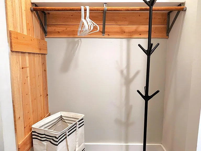 Dedicated entry nook with hardwood-style flooring, rustic wood accent wall, and open hanging rail with shelf for storage.