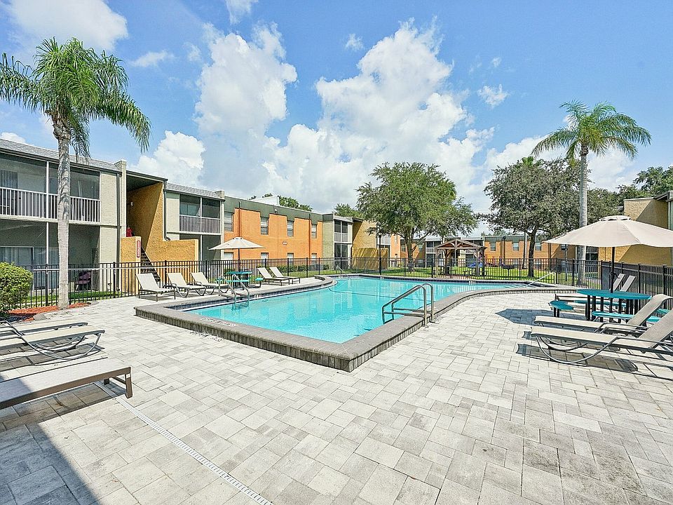 Charming apartment community with a sparkling pool, surrounded by modern lounge chairs and lush greenery under a clear blue sky.