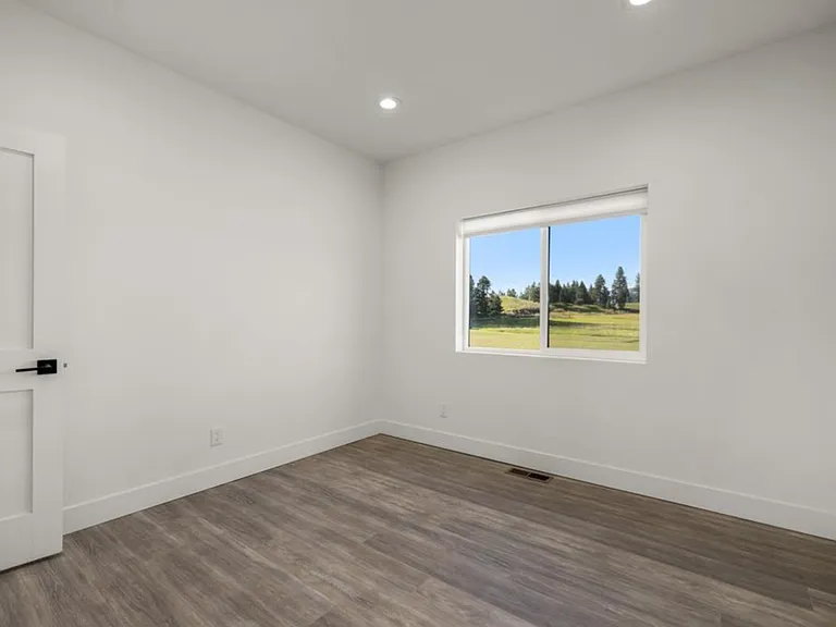 Bright and inviting first-floor bedroom featuring high ceilings, recessed lighting, beautiful modern flooring, and a large window overlooking the peaceful mountain range and surrounding Montana landscape.