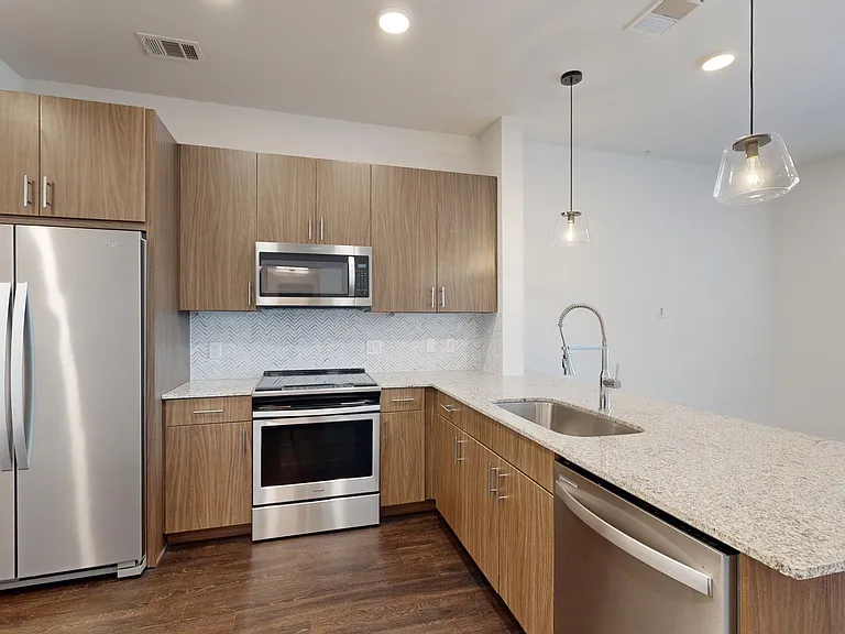 Apartment kitchen with stainless steel appliances, granite countertops, and wood-style flooring.