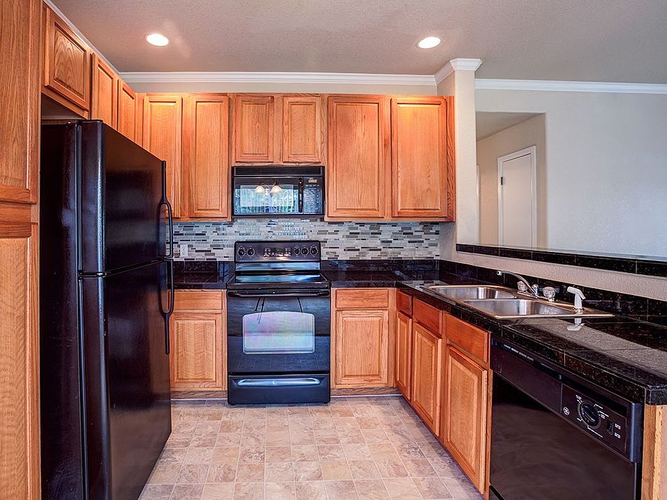 Kitchen featuring all black appliances, large Formica counter tops, and walnut cabinets.