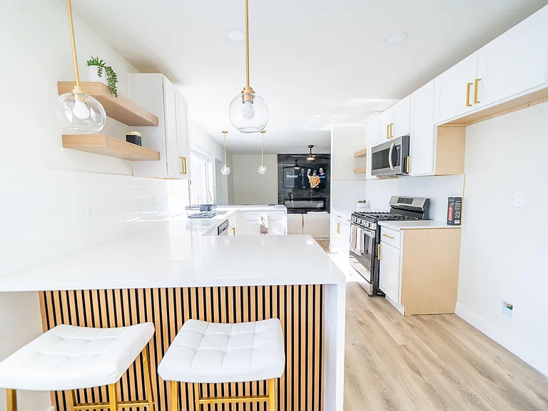 Open kitchen with peninsula seating, white cabinetry, quartz-style counters, and stainless steel range and microwave.