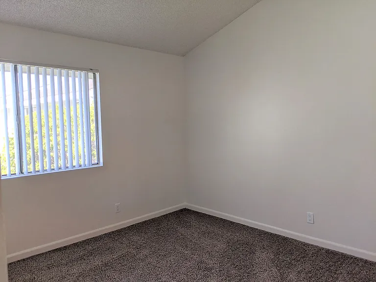 Carpeted bedroom with nice natural lighting and vertical blinds in apartment unit at the Steckel Apartments in Santa Paula, California.
