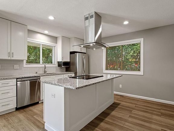 Brand new kitchen with high-end appliances, glass backsplash, granite counters, island with glass vent hood.