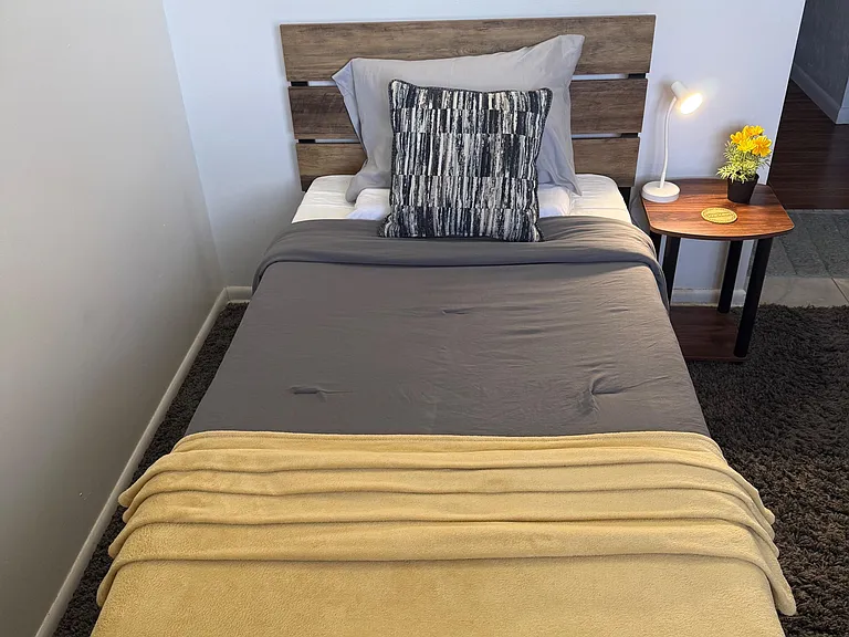 Furnished bedroom with a comfortable bed, wood headboard, bedside table with lamp, and soft area rug.