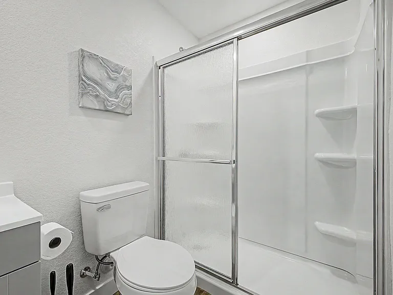 Clean bathroom featuring a tub/shower combo with sliding glass doors, built-in shelving, and a modern vanity.