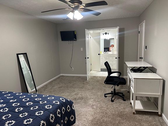 Carpeted bedroom with ceiling fan, wall-mounted TV, and a desk setup, plus convenient access to an en-suite vanity area.