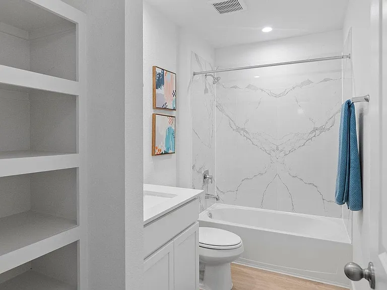 Bathroom offers a tub/shower combo with marble-look surround, vanity sink, and built-in shelving for added storage.