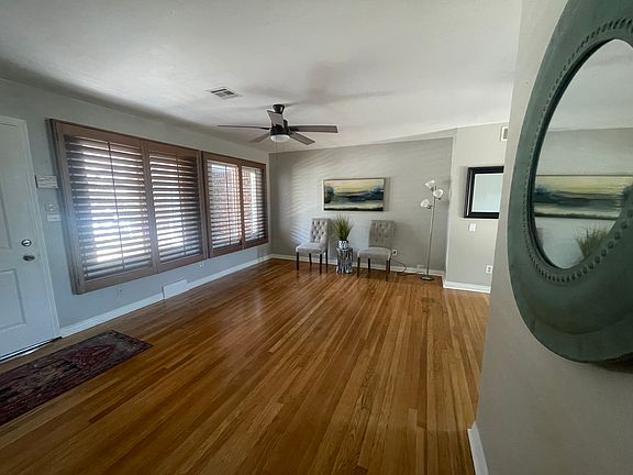 Living room with plantation shutters, wood floors, ceiling fan,
