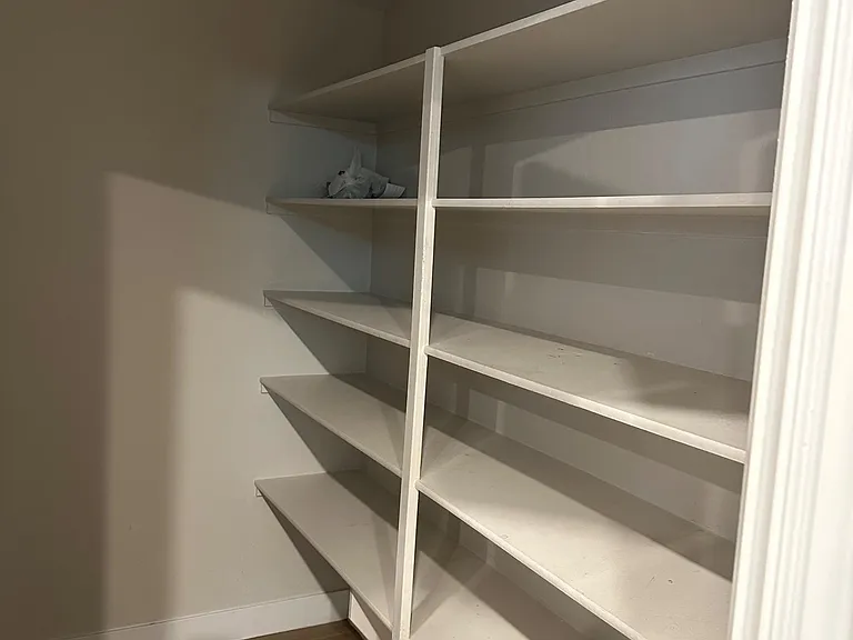 Walk-in storage room with built-in shelving for pantry items, linens, and household supplies, plus durable flooring.