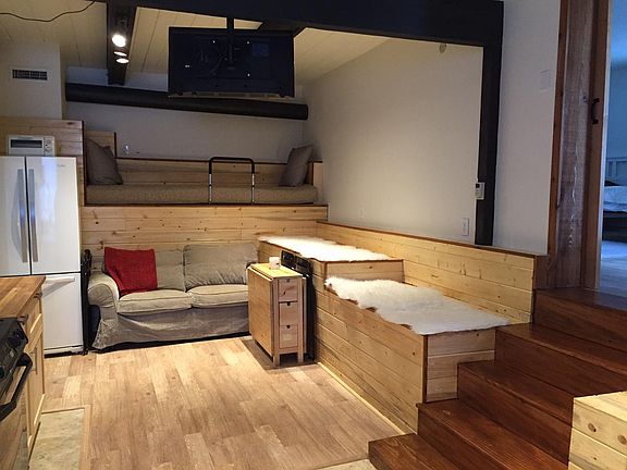 Living room by the kitchen: extra bed on top of the couch, winged table, folding chairs; smart TV hanging from the ceiling