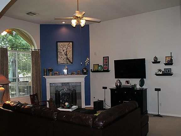 Family room with corner fireplace and gas logs, accent wall, high ceilings and ceiling fan.