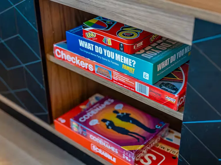 Open shelves beneath the TV showcase a charming selection of neatly stacked board games, thoughtfully curated to ensure guests have everything needed for memorable bonding moments with family and friends.