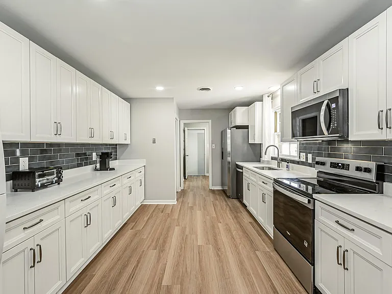 Spacious galley kitchen with ample white cabinetry, solid-surface counters, and stainless steel appliances for easy meal prep