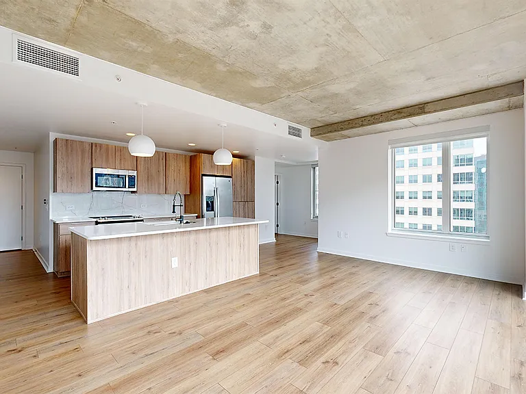 Apartment kitchen with stainless steel appliances, dining and living room with wood-style flooring.