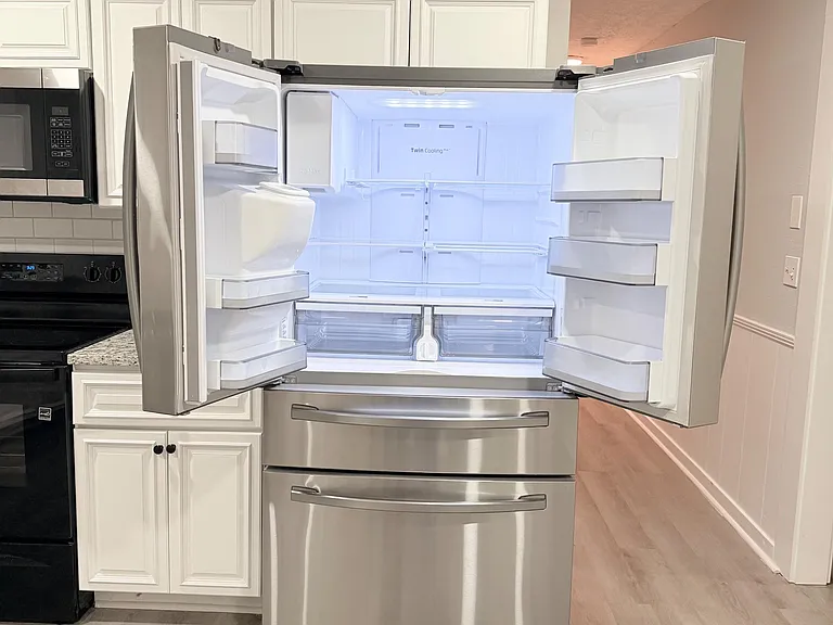 Kitchen with stainless French-door refrigerator, ample white cabinetry, and durable counters for everyday meal prep.