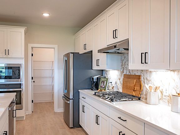 Kitchen with pantry, appliances, white cabinetry and accent patterned backsplash and gas range