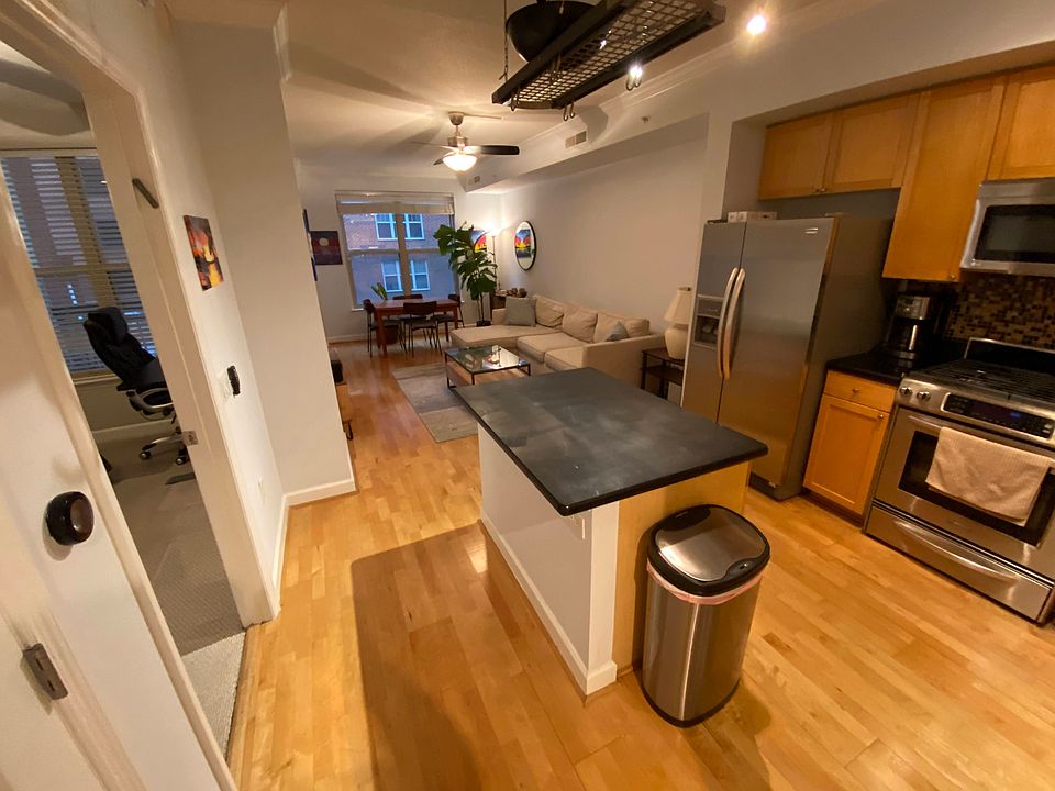 Open concept kitchen with granite countertop island, hanging pot rack, and stainless steel appliances - including a gas stove.
