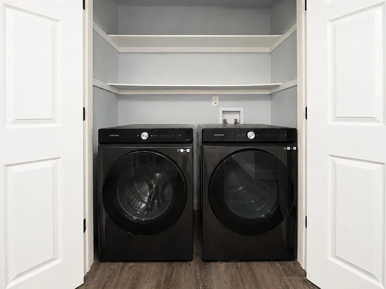 Dedicated laundry closet with front-loading washer and dryer plus built-in shelving for detergents and linens.