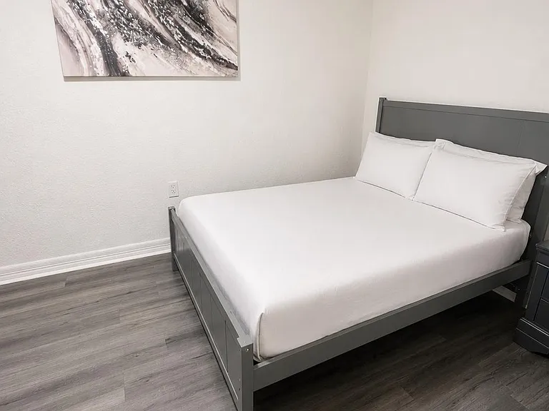 Furnished bedroom with a full bed, nightstand, and durable wood-look flooring, offering a clean and comfortable setup.