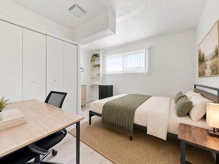 Well-appointed bedroom with a dedicated desk, large closet, and window with blinds plus open shelving and mini fridge.