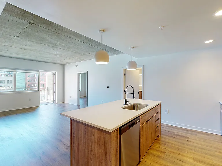 Apartment kitchen with stainless steel appliances, dining and living room with wood-style flooring.