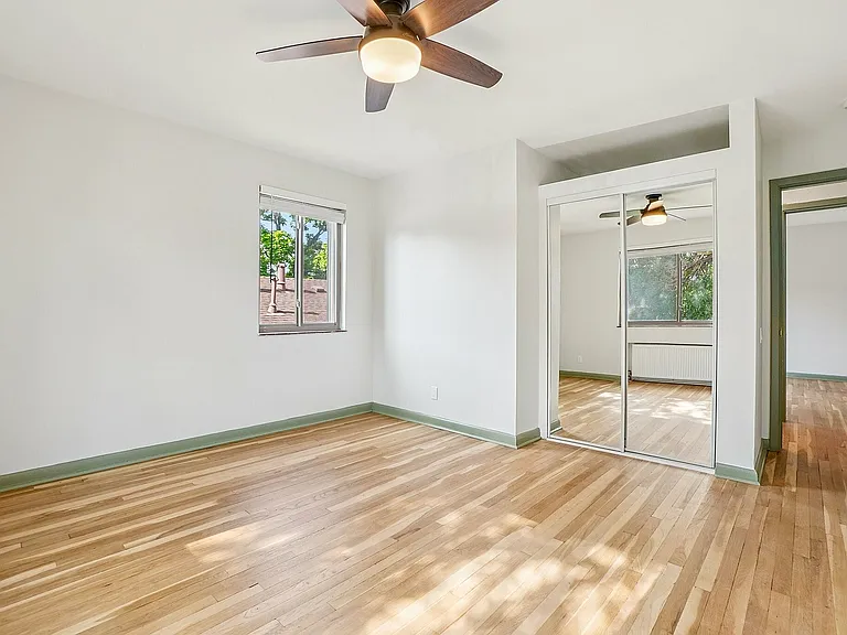 Bright and airy room with elegant hardwood flooring, ceiling fan, and large mirrored closet doors overlooking a scenic outdoor view.