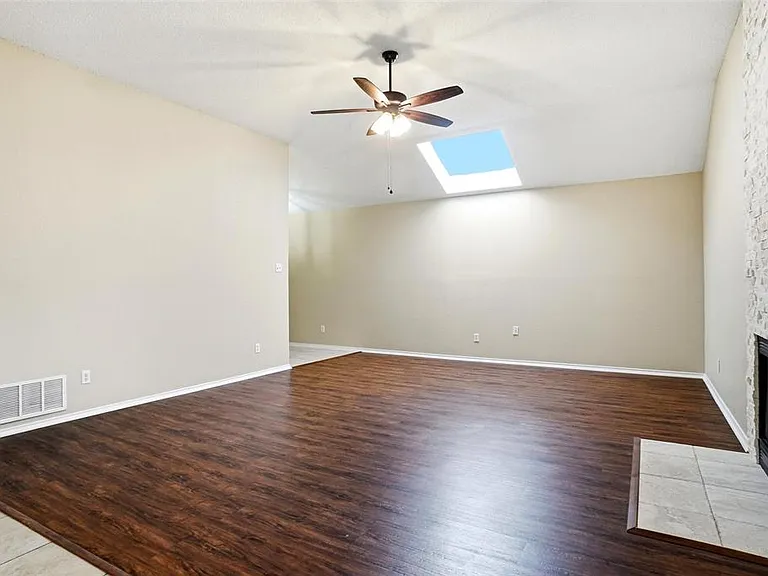 Spacious living area featuring wood-finish flooring, a white brick fireplace, and a skylight
