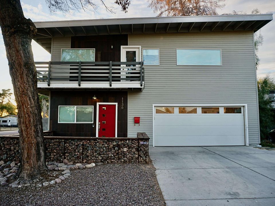 Front of the home with courtyard area surrounded by gabion wall, 2 car garage, and upstairs balcony that wraps around to overlook the backyard.