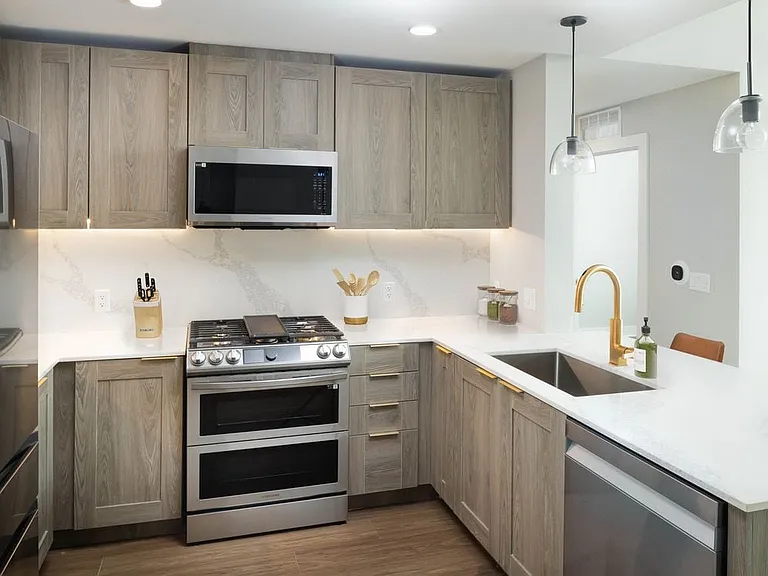 Signature Collection kitchen with stainless steel appliances, marbled white quartz countertops, brown cabinetry, and hard surface flooring