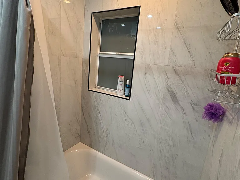 Full bath with tiled tub/shower surround, recessed lighting, window for ventilation, and built-in shower storage.