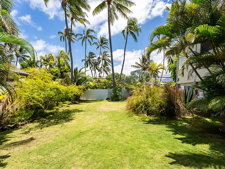 Expansive grassy yard surrounded by mature tropical landscaping, offering a private outdoor setting perfect for relaxing or entertaining.