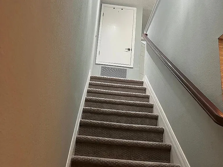 Stairs leading to bedroom hallway and facing closet containing iron and ironing board and air conditioner blower