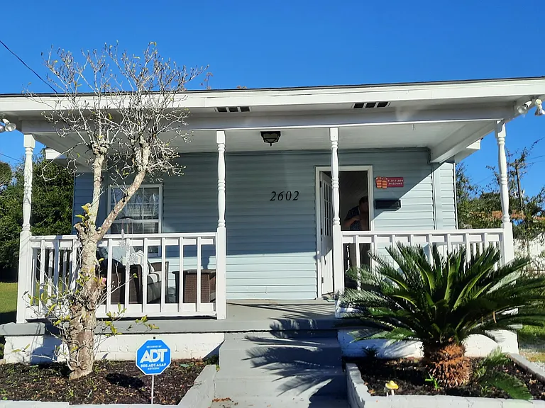 As well as this frontal view, the back porch is similar in size. The large back yard includes a make shift fire pit in the ground, coal barbeque and very large table.