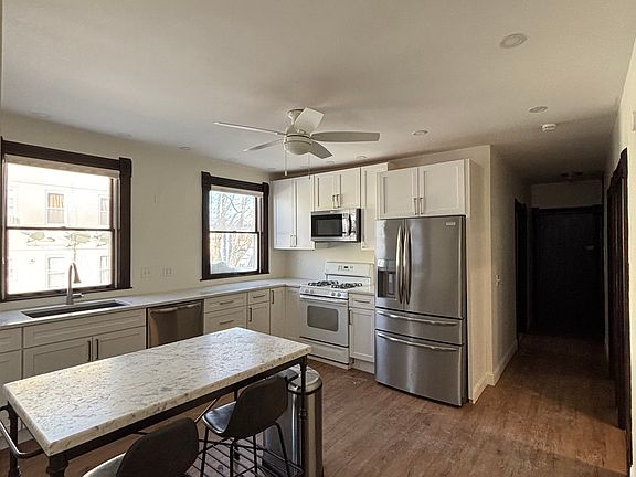 Alternate view of the modern kitchen showcasing the marble island, included chairs, and generous counter space. Great natural light and a functional layout ideal for everyday living.