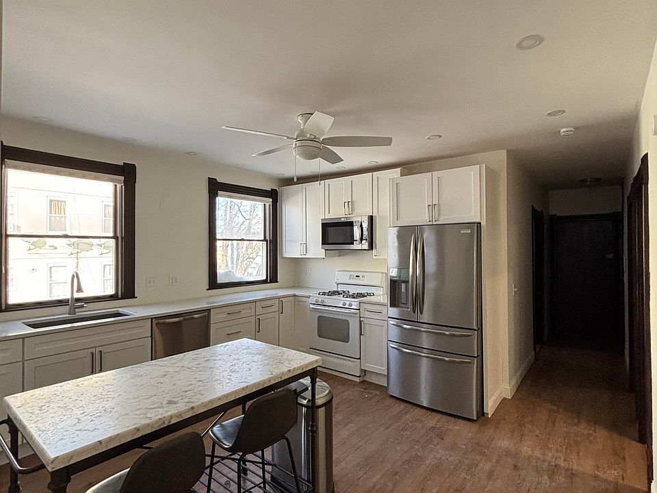 Alternate view of the modern kitchen showcasing the marble island, included chairs, and generous counter space. Great natural light and a functional layout ideal for everyday living.