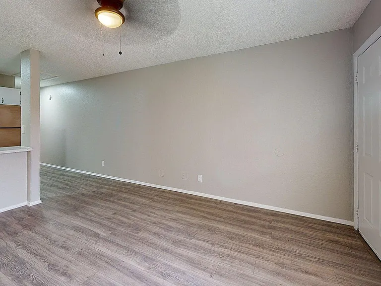 Elegant apartment interior with modern gray walls, sleek ceiling fan, inviting laminate wood flooring, and a stylish open kitchen with stainless steel appliances.