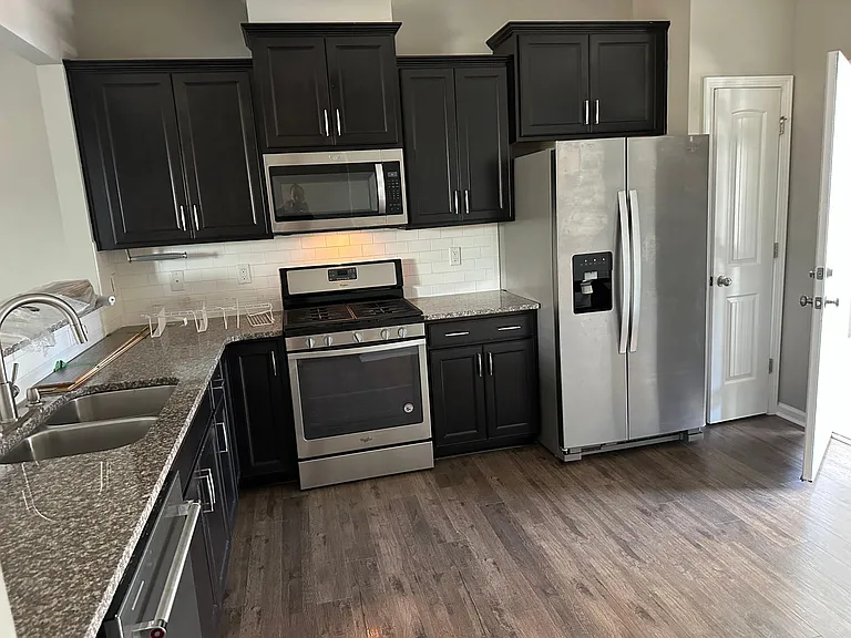 A view of the kitchen, which includes a gas range, a refrigerator, a microwave, and a new top of the line dishwasher . The open door is the garage door, the closed door is the pantry.