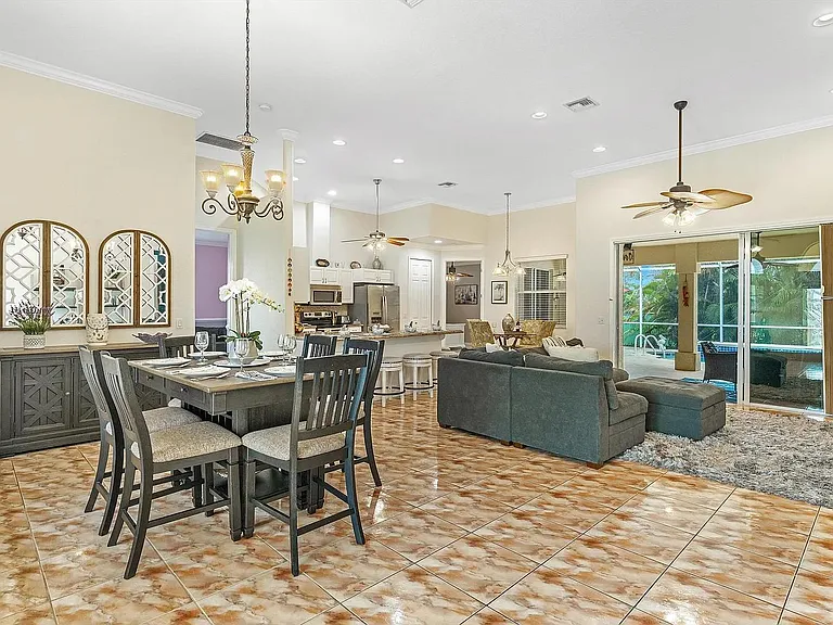 Open-concept living and dining area with tile floors, ceiling fans, sofa and sliding doors to the pool and lanai.