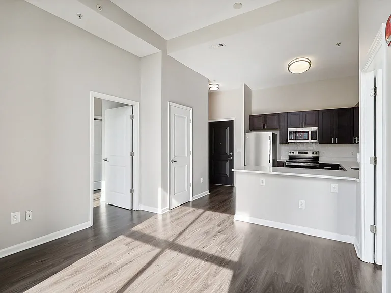 the living room and kitchen of a apartment with white walls and wood floors
