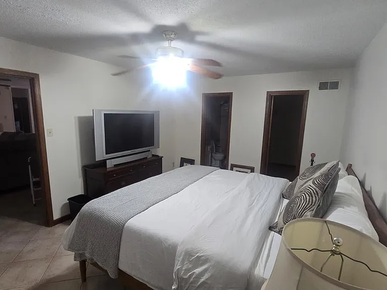 Furnished bedroom with a ceiling fan, TV/dresser setup, and convenient access to adjacent rooms.