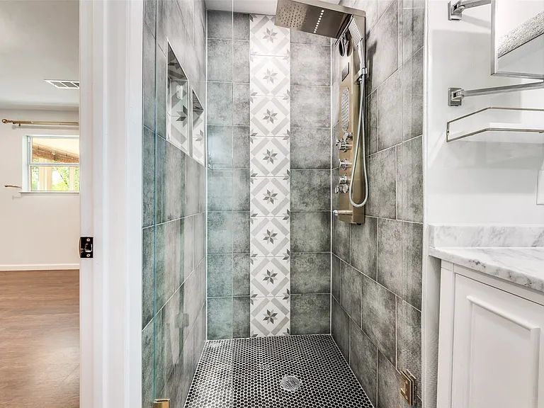 Walk-in shower with textured gray wall tiling and decorative accent tile