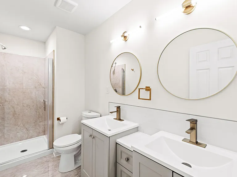 Bathroom with a double-sink vanity, round mirrors, and a glass-enclosed shower with tiled surround.