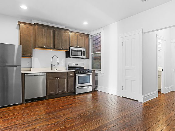 Kitchen looking into the hallway to the bathroom, laundry, and bedroom, salvaged hardwood floors, full stainless steel appliance package with gas oven and microwave, commercial-style kitchen faucet, high-end quartz countertops