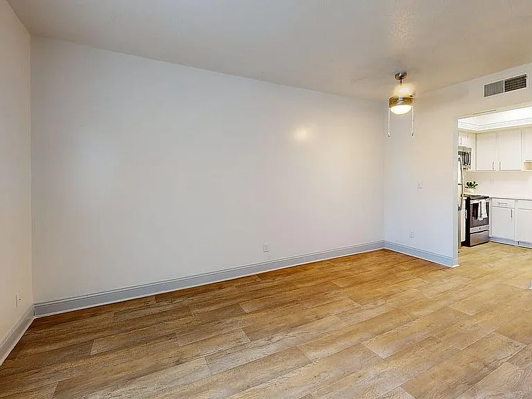 Inviting open-concept living and dining area with elegant wood flooring, bright walls, and a modern ceiling fan, leading to a sleek kitchen.